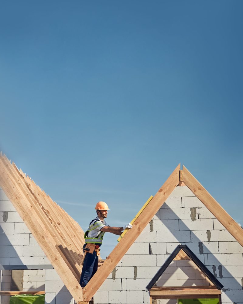 Professional construction worker using a level to measure the right angle of the house roof