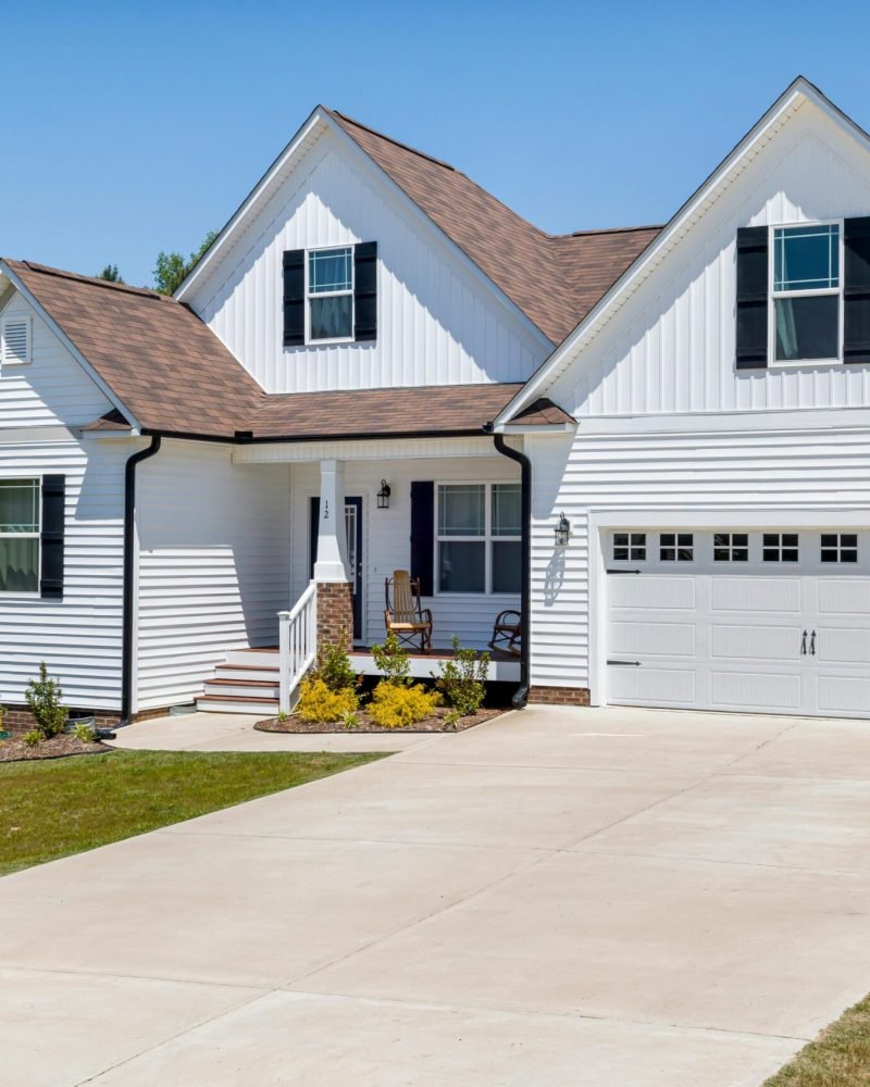 Modern white two-story home with black shutters, attached garage, and concrete driveway in a suburban neighborhood